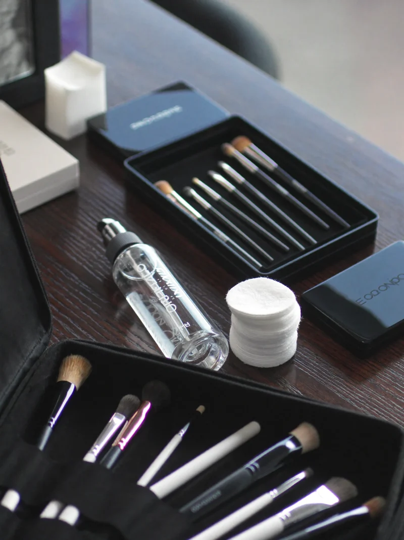 Ordnet makeupkit med pensler, sanitering og vatrondeller på et træbord